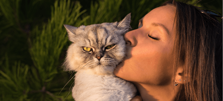 A woman kisses an annoyed cat.